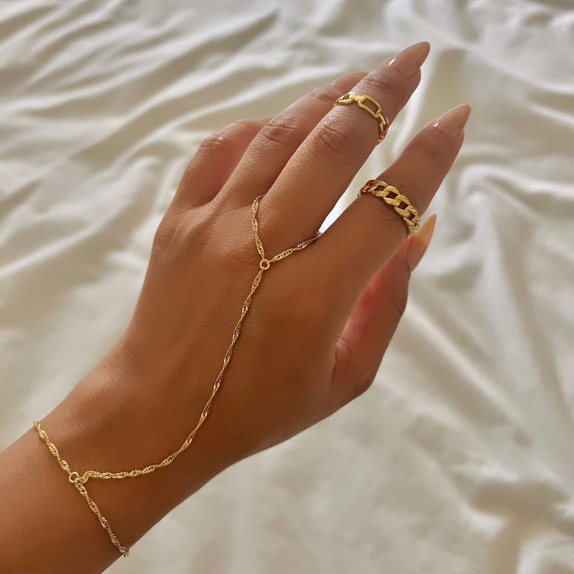 A person's hand wearing a gold-colored chain bracelet with a singapore chain design.