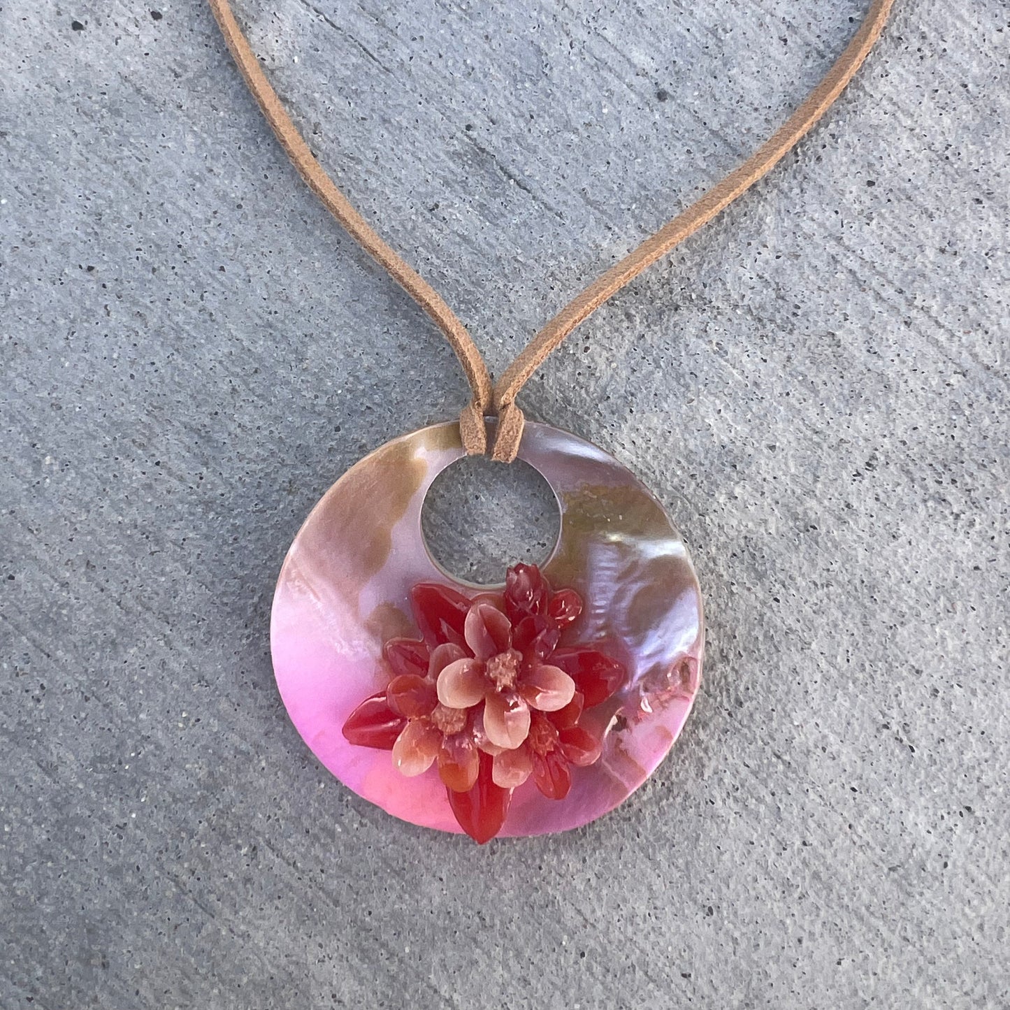 Necklace with a pink pendant featuring a floral design on a concrete surface