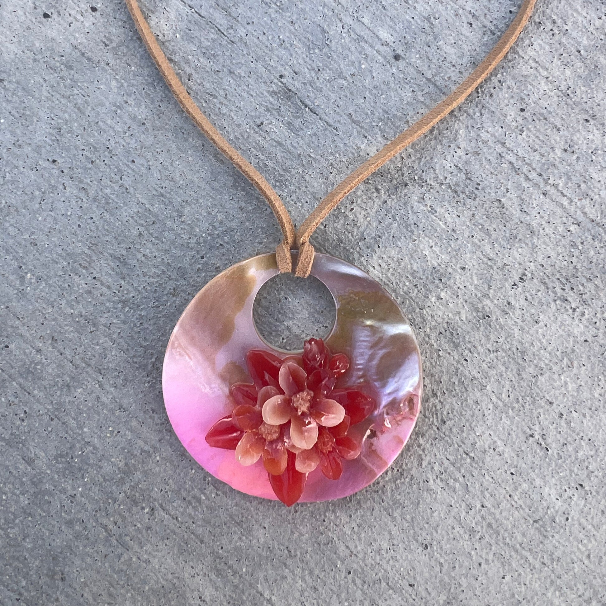 Necklace with a pink pendant featuring a floral design on a concrete surface