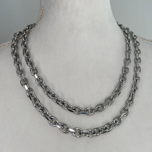 Silver chain necklace on a mannequin arm against a gray background
