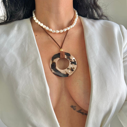 Person wearing a white blazer with a necklace featuring a large circular pendant.