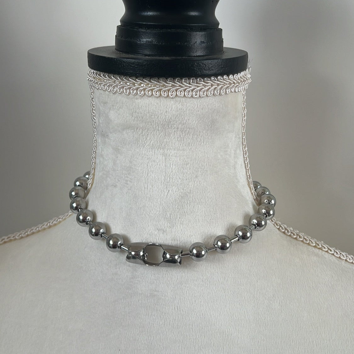 A silver-colored ball chain choker necklace displayed on a mannequin.